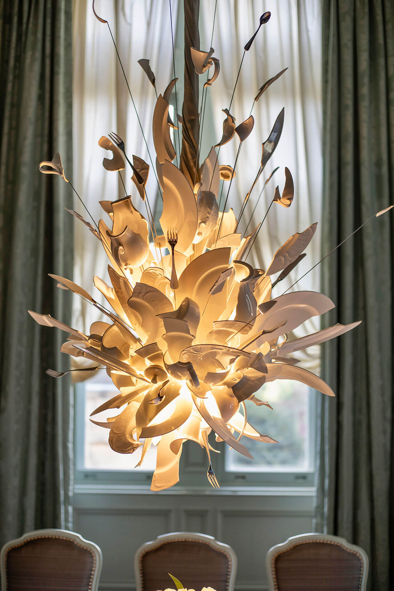 Decorative chandelier from Ingo Maurer hanging above a table with chairs in a room with curtains.