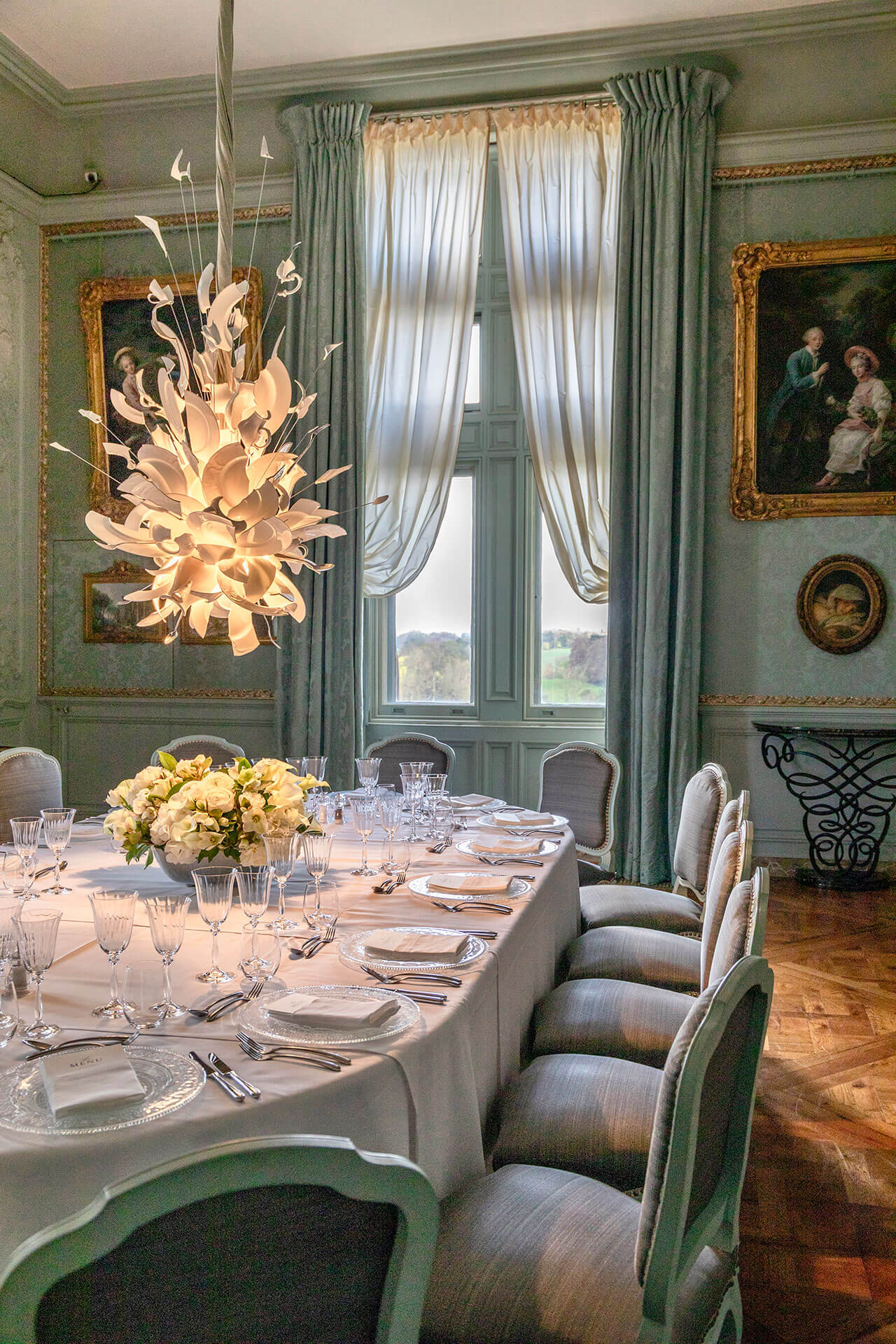 Elegant dining room with a long table set for dinner, floral centerpiece, and Ingo Maurer lighting at Waddesdon.