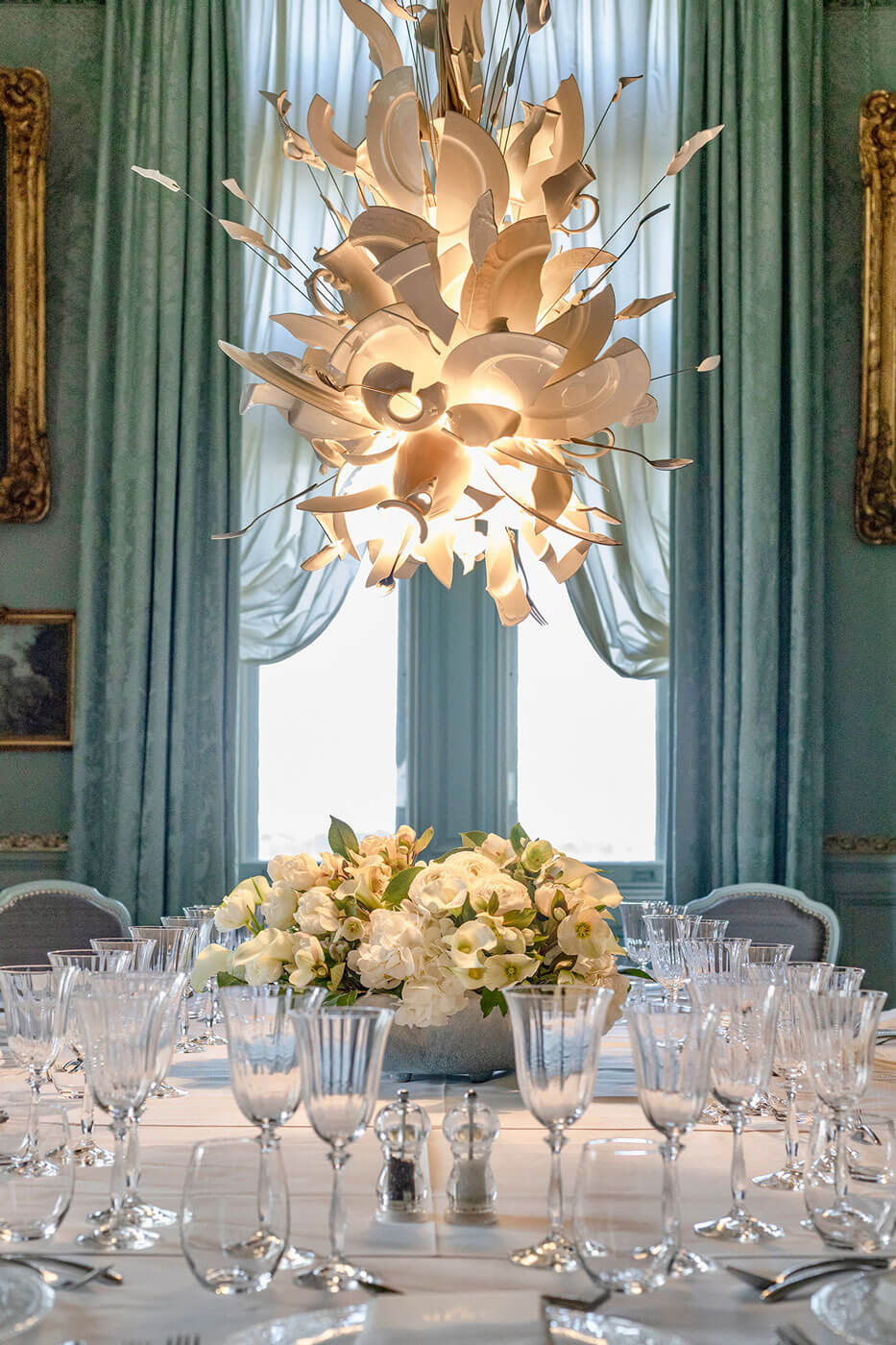 Elegant dining room with a hanging chandelier from Ingo Maurer and a table set with glasses and flowers.
