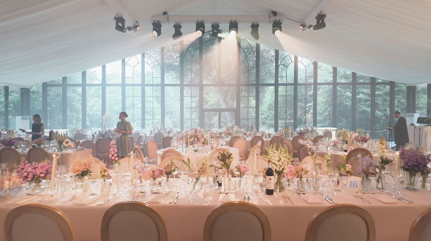 Large marquee with tables set for a formal event, large windows in the background.