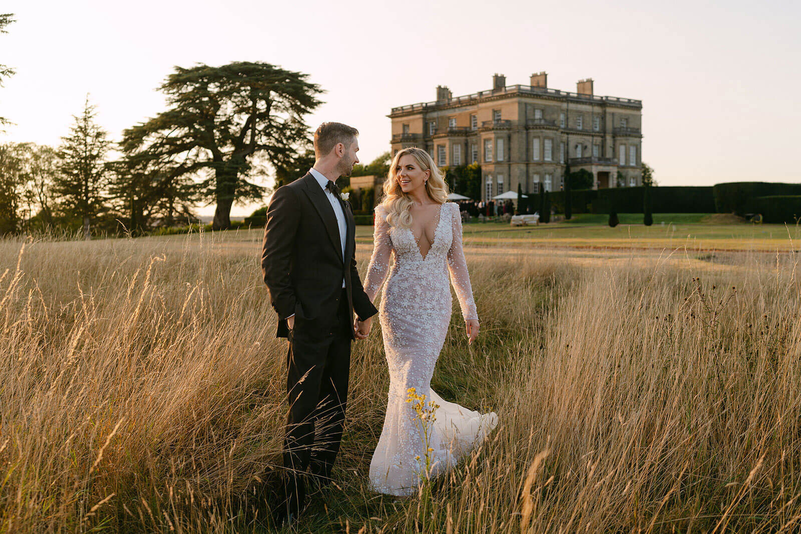 Bride and groom in standing in a field with a large stately home in the background