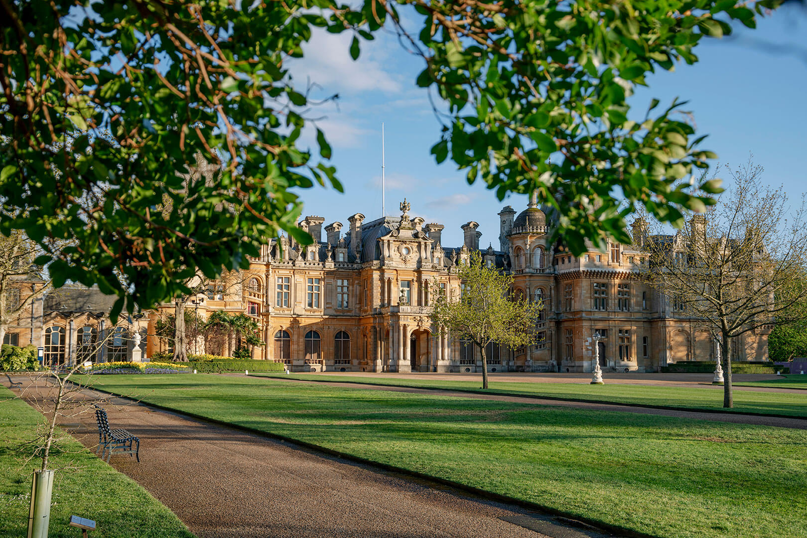 Large mansion with a grand entrance, surrounded by greenery and a clear sky.