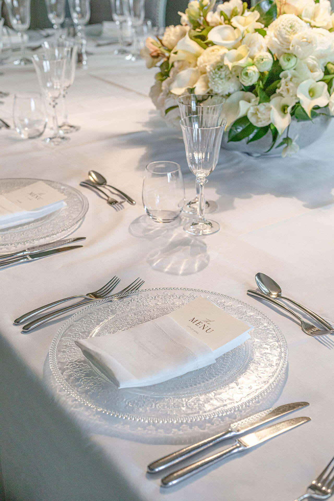 Elegant table setting with clear glassware, silver cutlery, and white flowers.