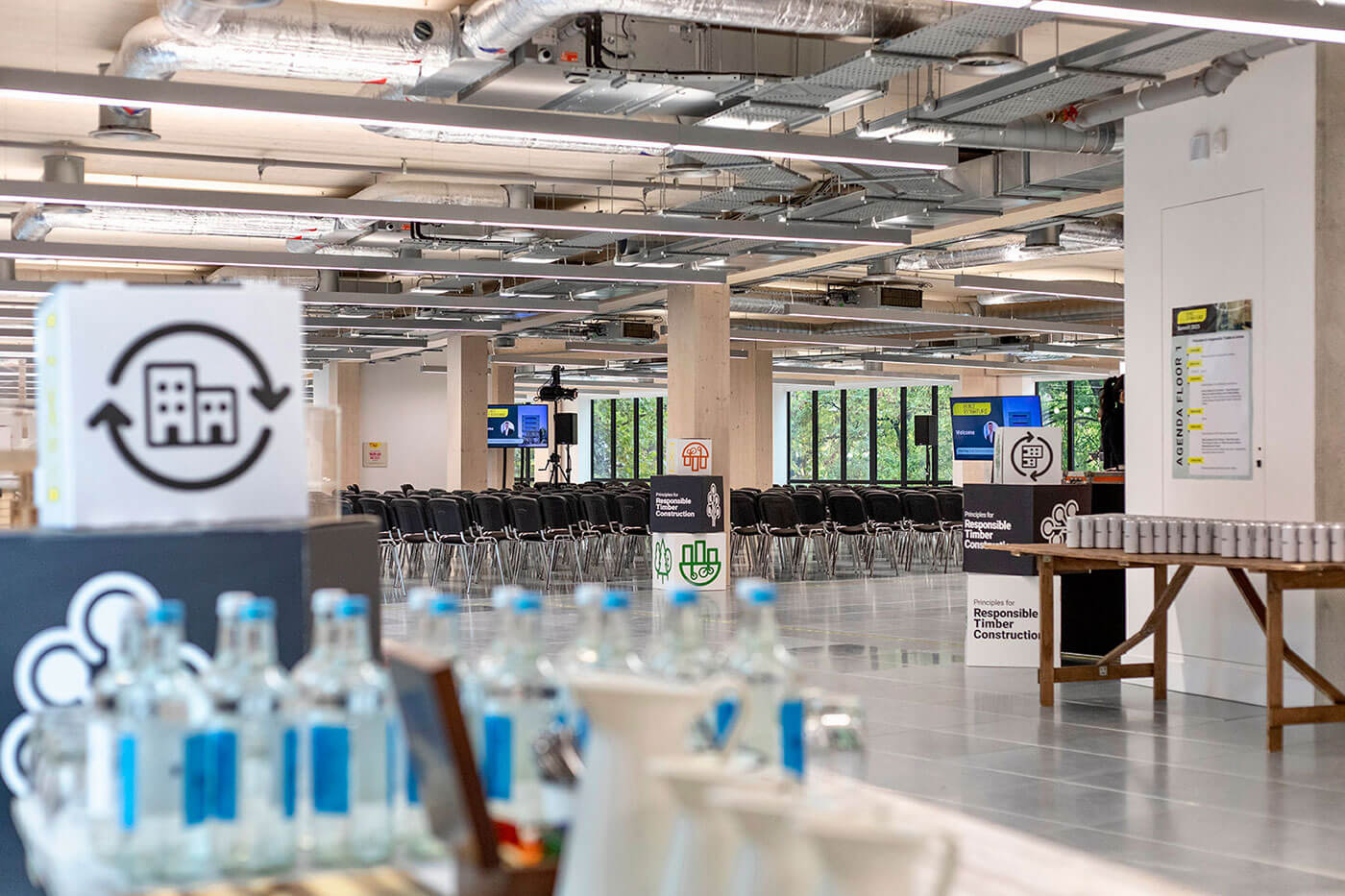 Large indoor conference space with tables and chairs, glass water bottles and cans of water