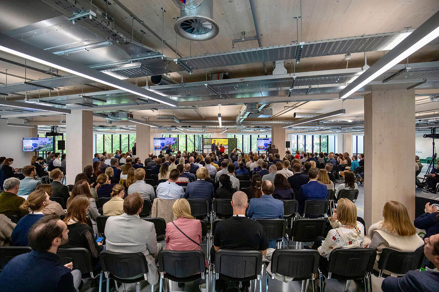 Large conference room in a timber building with attendees facing a stage with screens