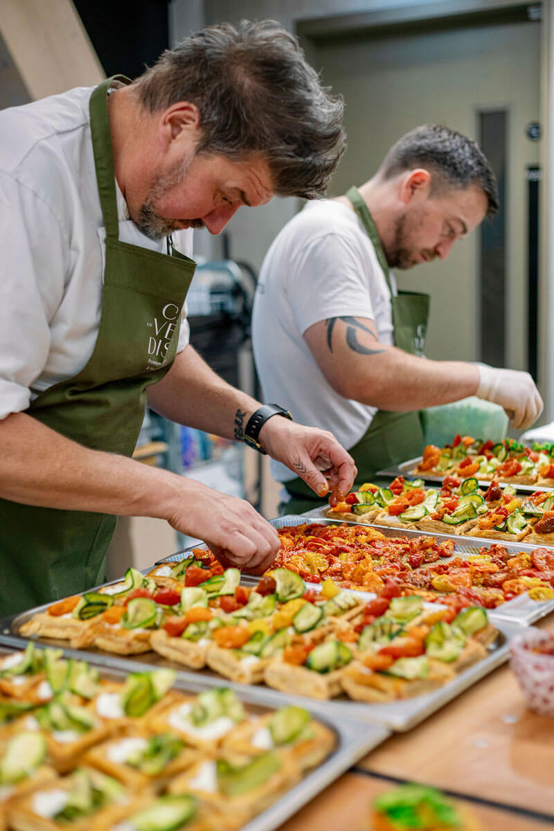 Two chefs preparing plant based dishes in a kitchen.