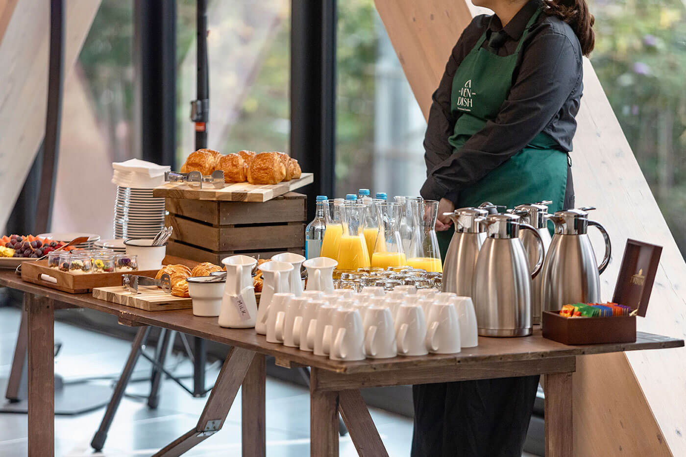 Person standing behind a table with coffee and pastries